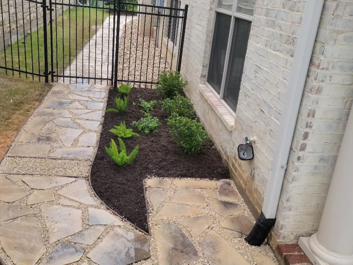 A small flagstone walkway and landing with some plants for a home with brick siding painted white