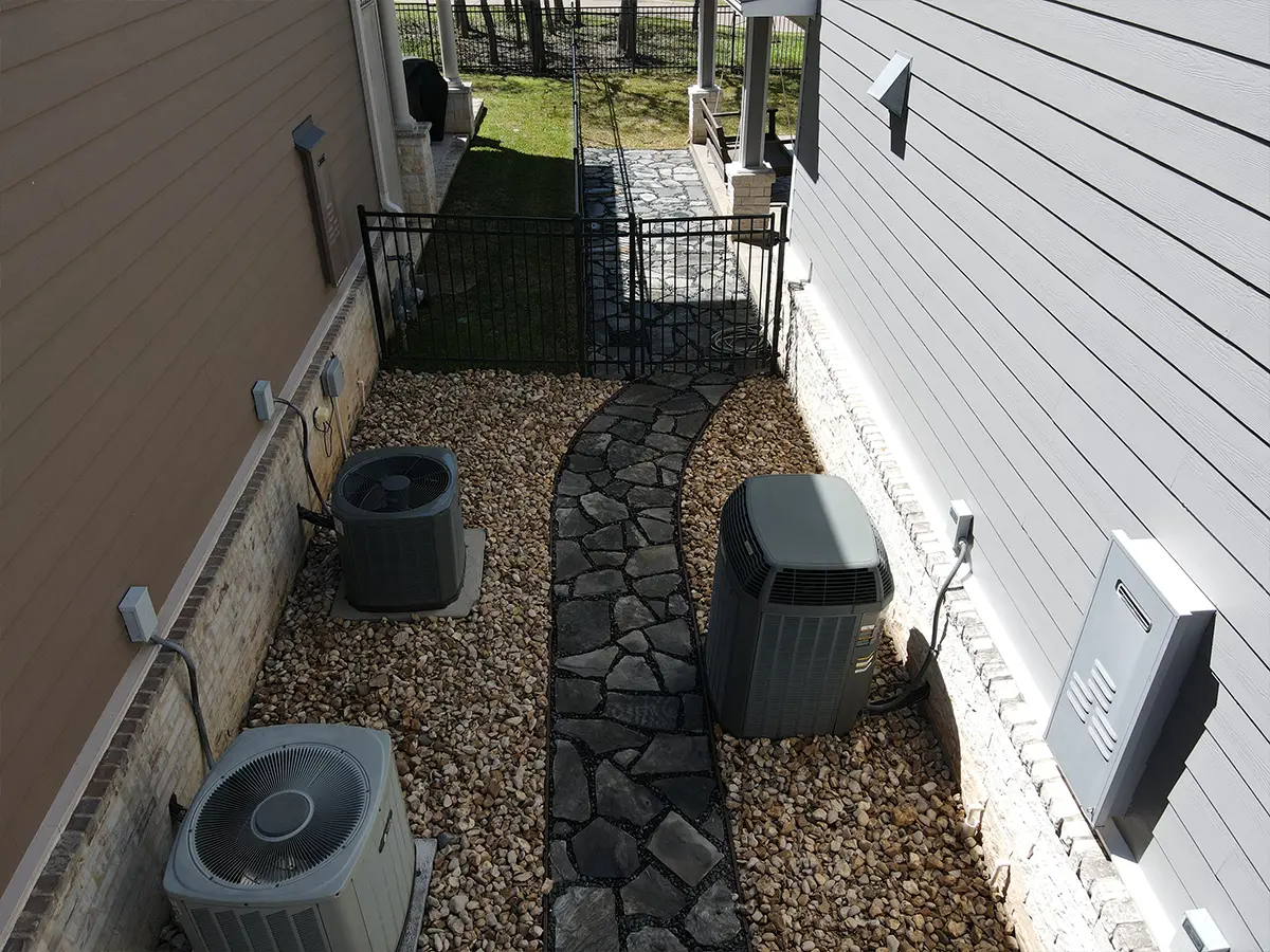 A nice concrete walkway surrounded by pebbles and rocks and a small aluminum fence with a gate separating two properties