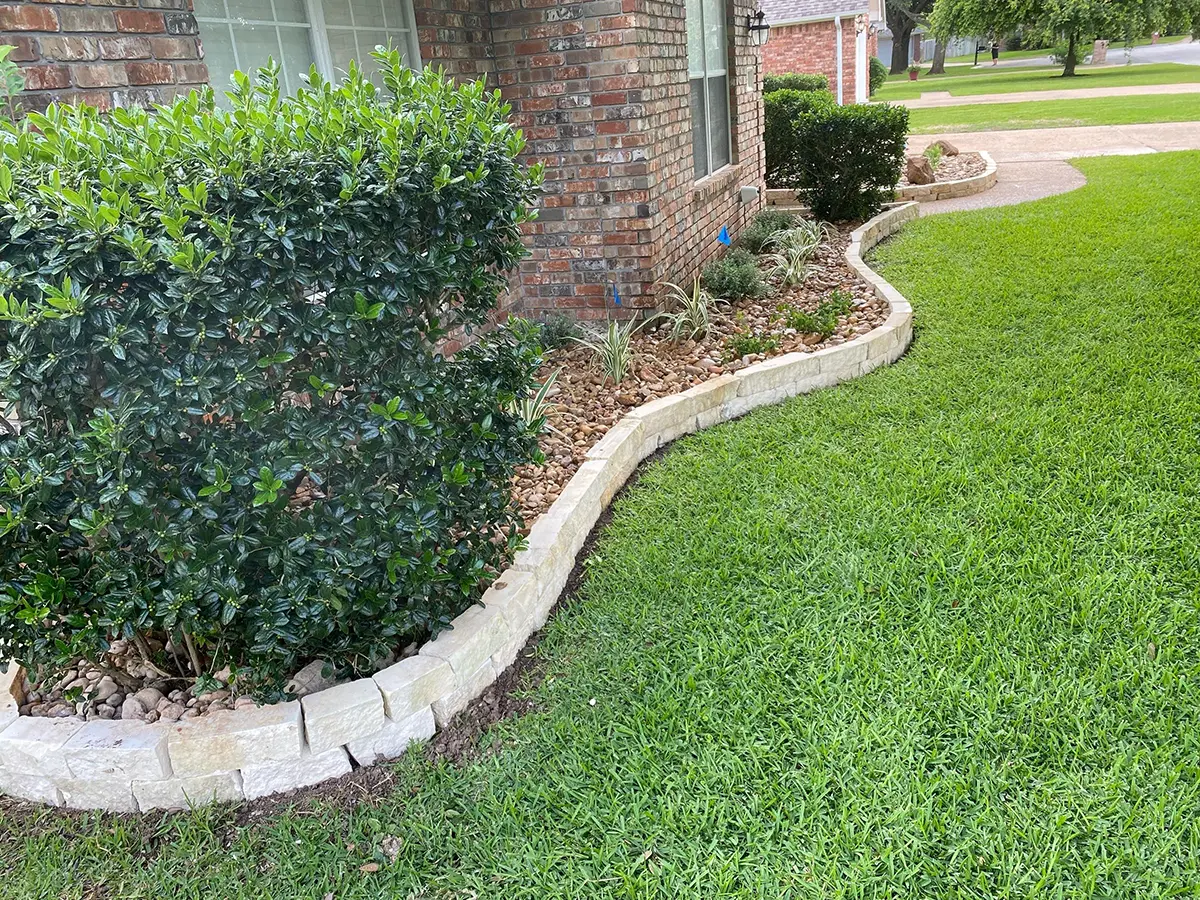 A lawn with a small landscape, brick edging, pebbles and rocks, and xeriscaping plants