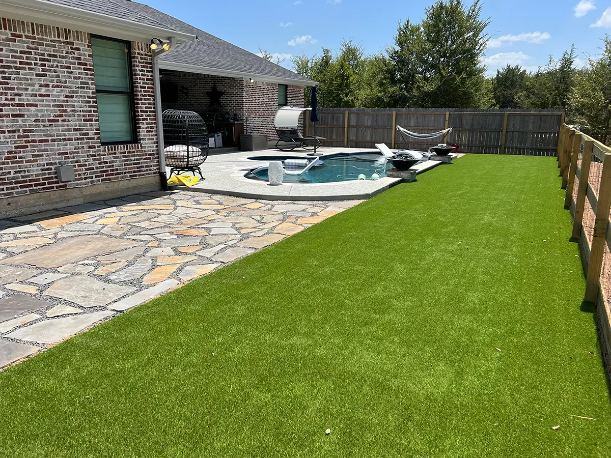 A lush patch of grass, flagstone patio, and concrete patio with a small pool