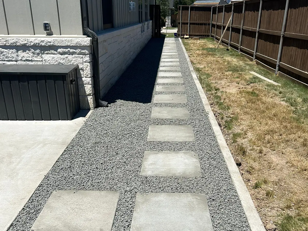 A patch of dried grass with a concrete walkway and gravel