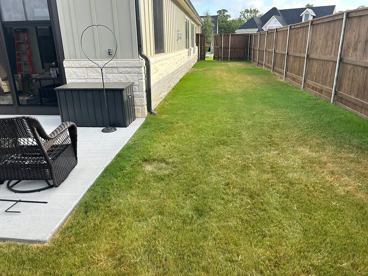 A patch of grass and a concrete patio with outdoor furniture