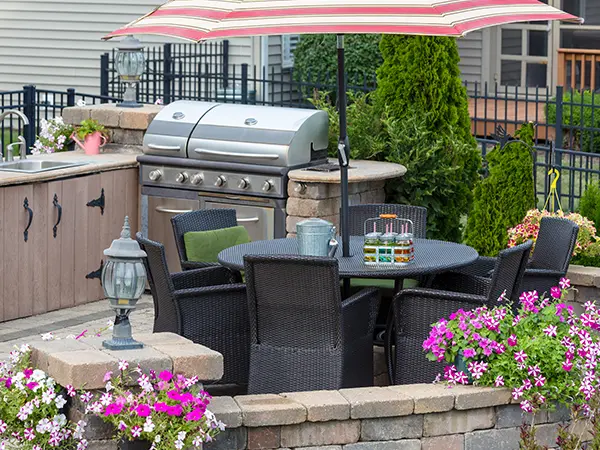 An outdoor kitchen with furniture, a grill, a retaining wall, and flowers
