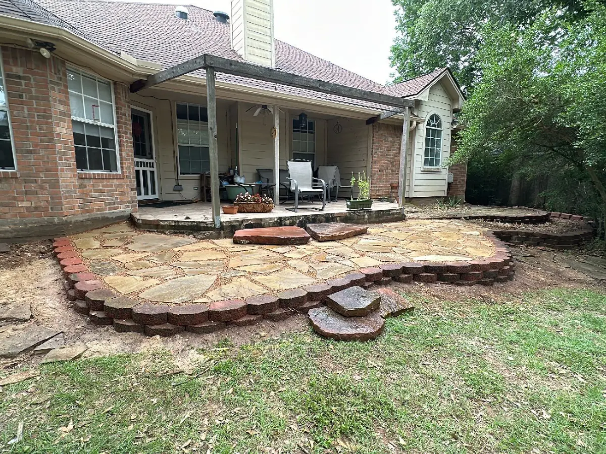A large patio with flagstone, paver edging, and two large stones as steps