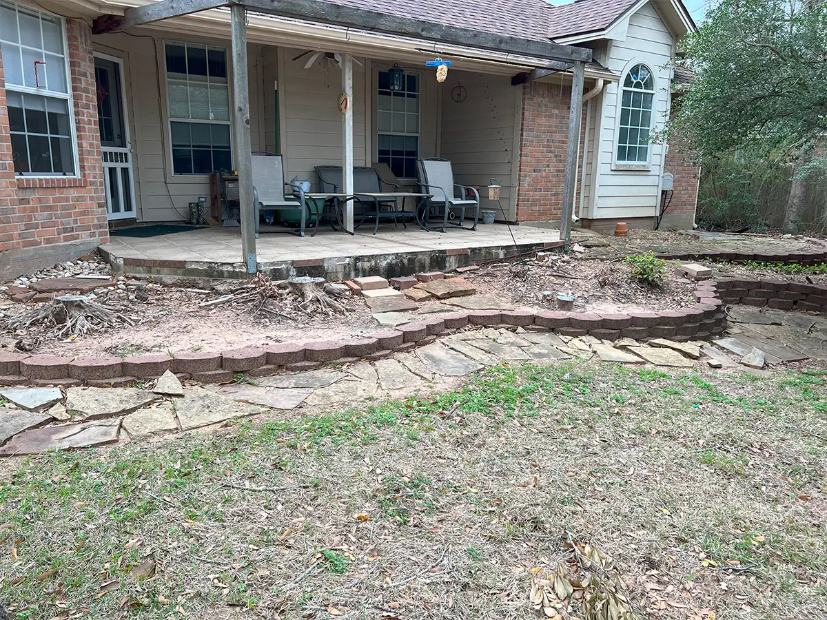 An unfunctional patio with pavers, dried grass and plants, and roots