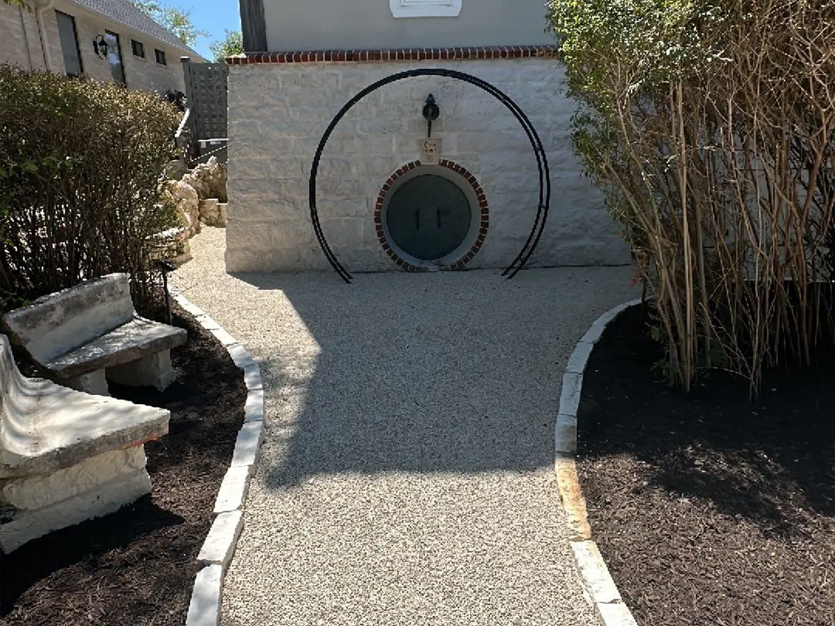 A clean walkway filled with gravel, two benches made of concrete, brick edging, and mulch