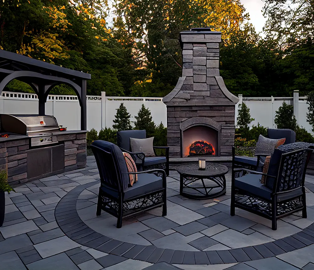 a beautiful paver patio with an outdoor kitchen and a tall fireplace