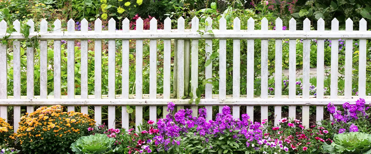 White picket fence surrounded by garden flowers
