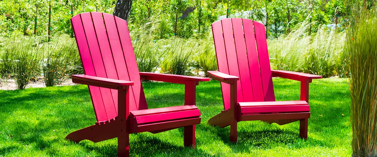 Traditional curveback sunset red polywood outdoor patio adirondack chairs with contoured backs and seats on green grass of outdoor lawn.