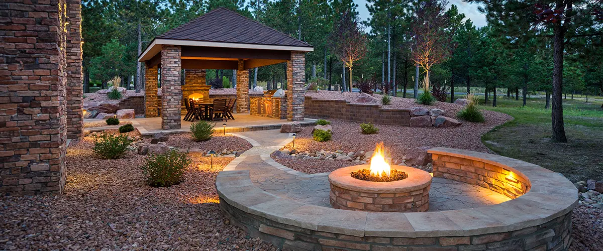 Stunning outdoor living space in beverly Estates, with stone fire pit, elegant lighting, and natural landscaping, ideal for evening gatherings and relaxation.