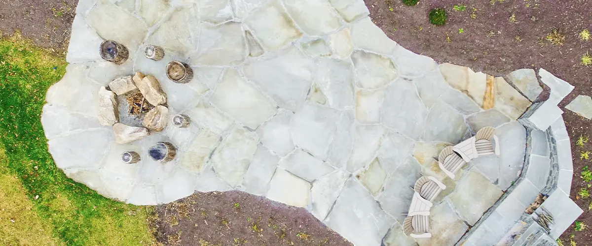 Aerial view of a backyard patio with a stone fire pit, seating area, and landscaping