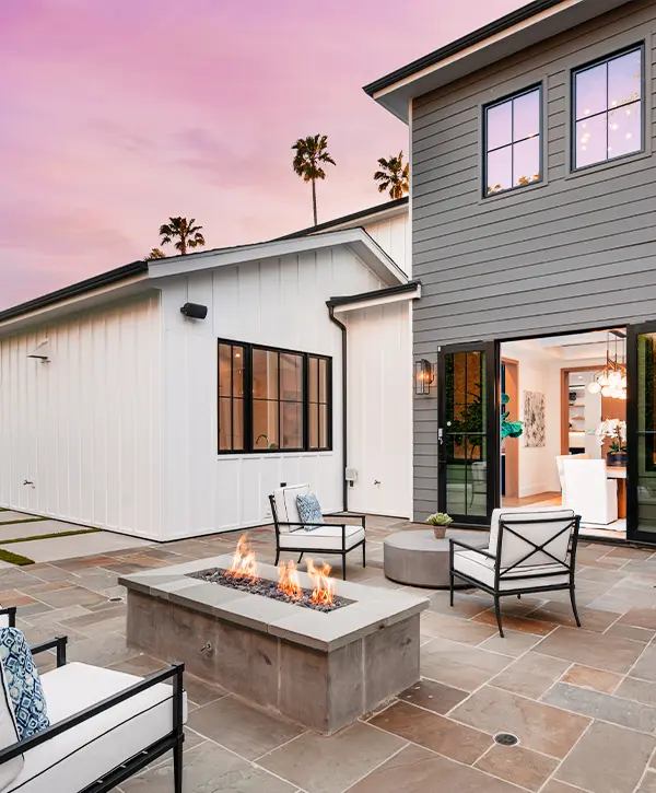 Modern backyard patio with fire pit, outdoor seating, and sliding doors at sunset