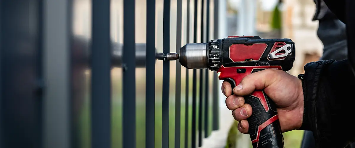 Close-up of a worker using a power drill to install a metal fence in Culpepper Manor, College Station, TX, highlighting precise craftsmanship in fencing installation.