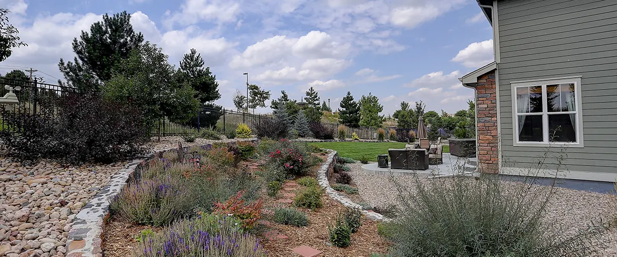 Spacious xeriscaped backyard in Culpepper Manor, College Station, TX, with stone-lined garden beds, lush greenery, and outdoor seating area, creating a serene landscape design.