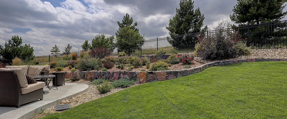 Xeriscaped Backyard in Culpepper Manor, College Station, TX, with tiered stone garden beds, vibrant plants, and cozy patio seating, offering a peaceful outdoor retreat under a cloudy sky.