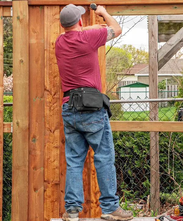 Worker securing wooden panels during a fence installation project