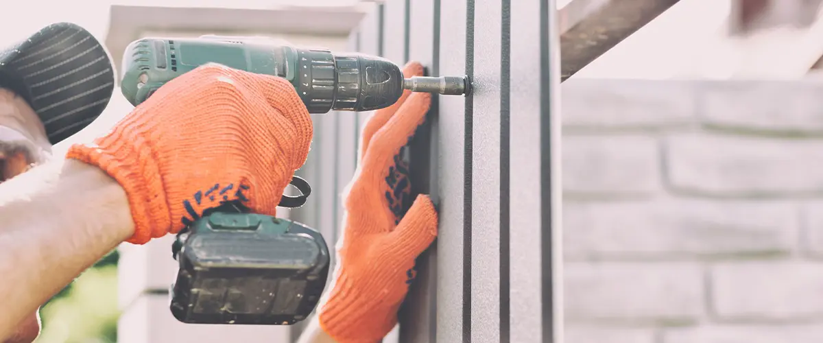 Close-up of a contractor using a power drill to install durable and modern fence panels with orange safety gloves.