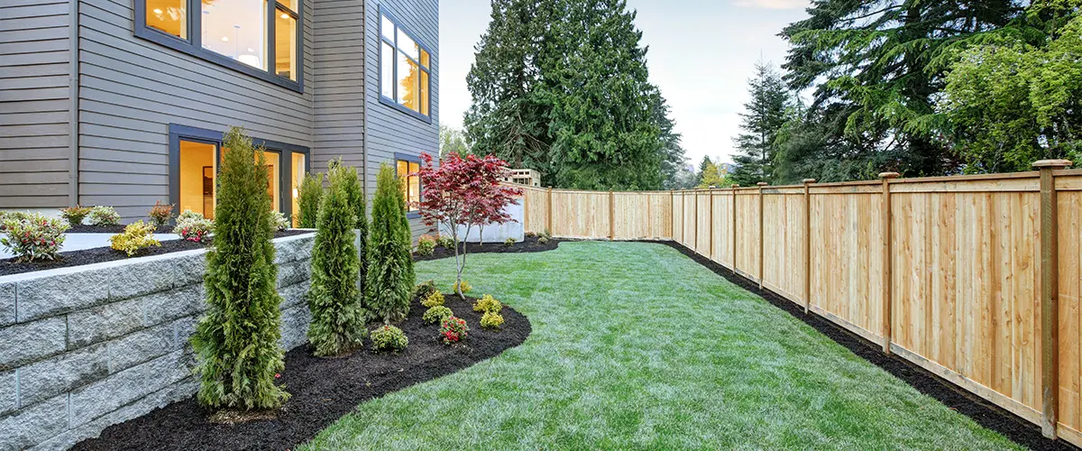 Modern backyard landscaping with fresh sod, vibrant plants, and a wood privacy fence enhancing curb appeal.