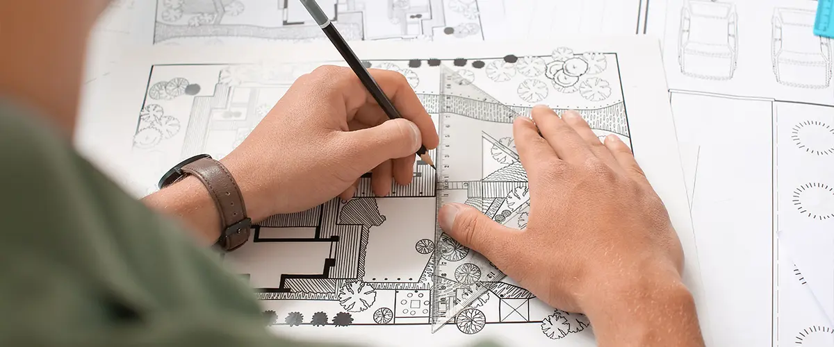 Architect drawing detailed landscape design plans with precision tools for a custom outdoor space.