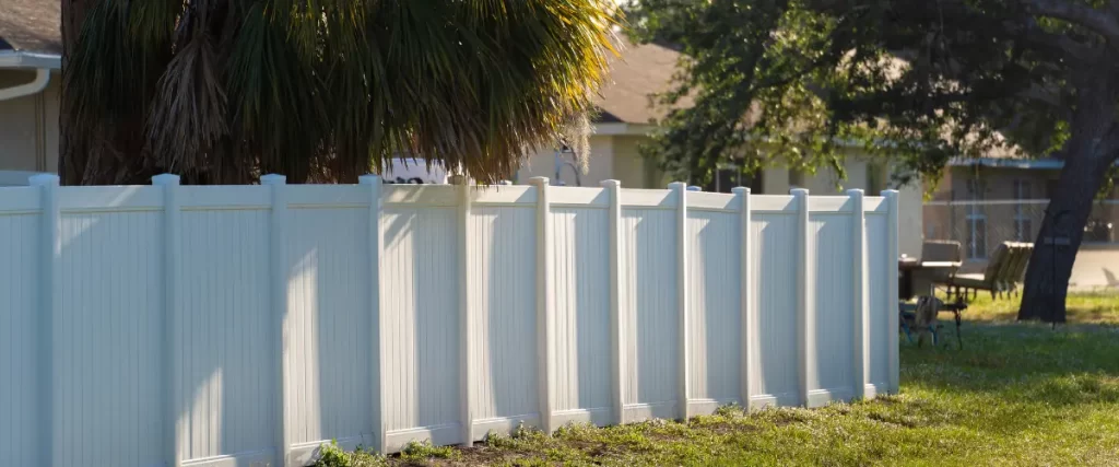 White vinyl fence in a backyard with palm trees and outdoor furniture