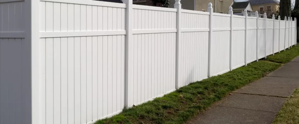 White vinyl fence with lush green trees and small shrubs