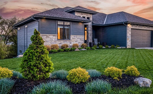 Modern home with professional landscape design, stone and dark siding, and a lush front yard at sunset