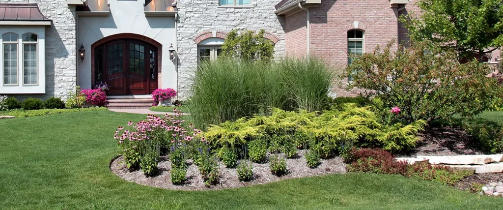 Beautifully landscaped front yard with manicured lawn, flowering plants, and stone elements in a suburban Bryan neighborhood.