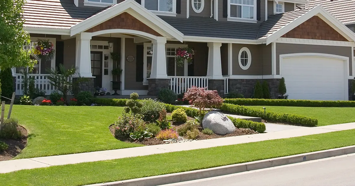 Modern front yard landscaping with ornamental grasses and flowering shrubs in front of a brick and stone Texas home