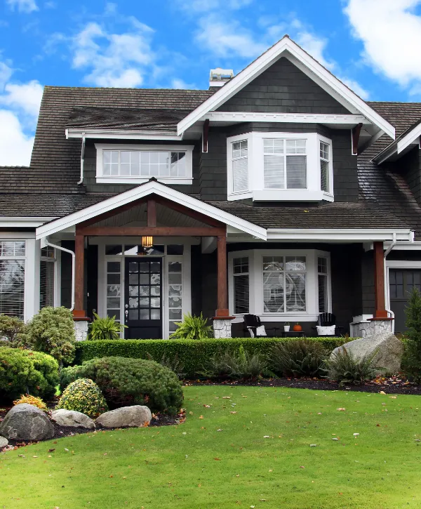 a large, two-story suburban house with a dark roof and siding and a well maintained landscaped front yard