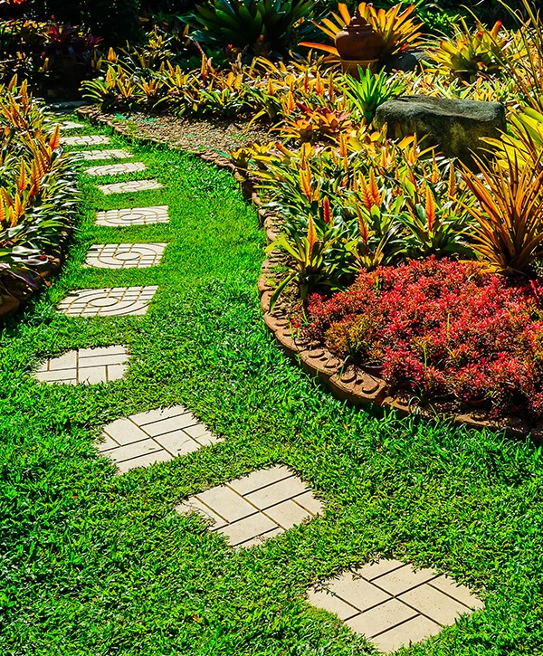 Colorful tropical garden landscaping with stone pathway, vibrant plants, and manicured lawn in a residential yard