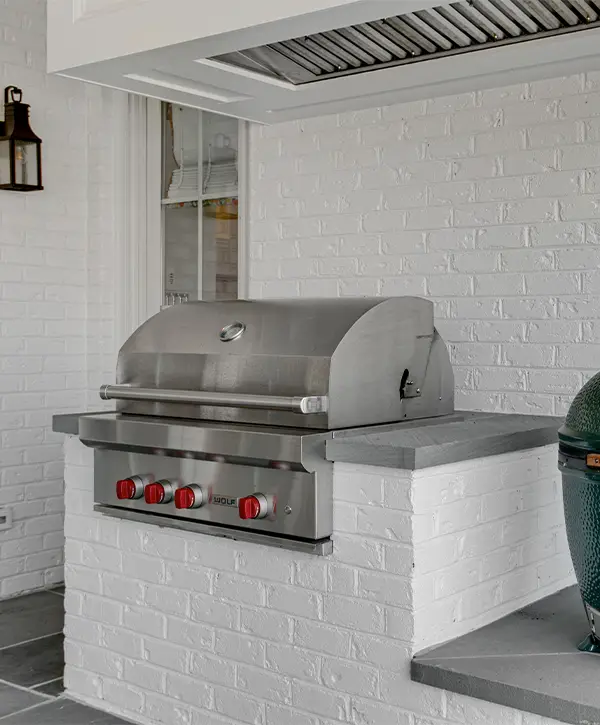 Built-in outdoor grill with brick kitchen island and stainless steel BBQ setup in a covered patio